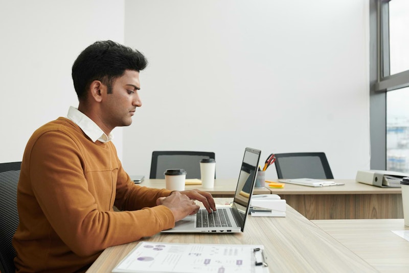 Man in an office building typing on a laptop