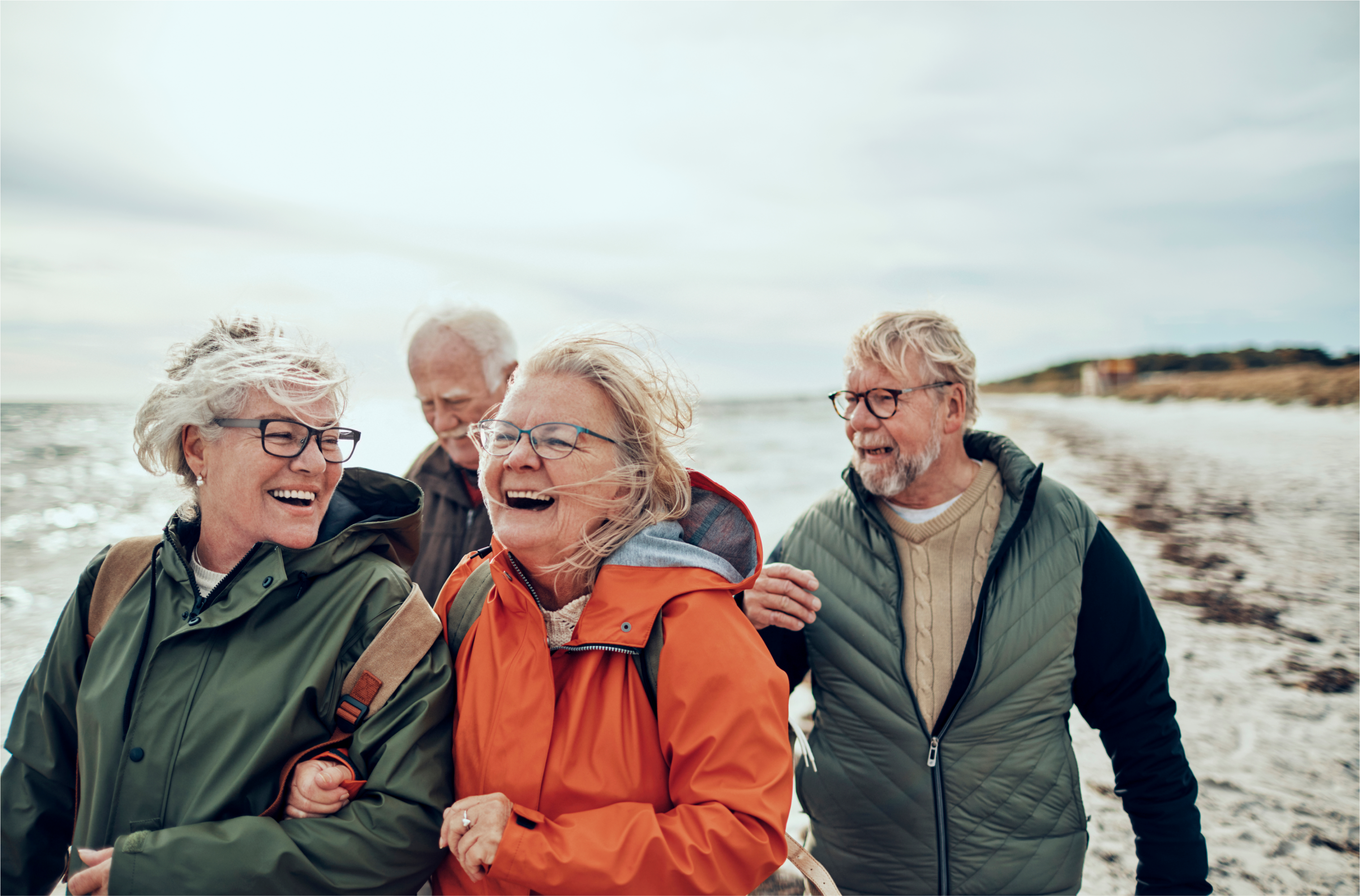 En grupp med fyra glada personer på en blåsig strand