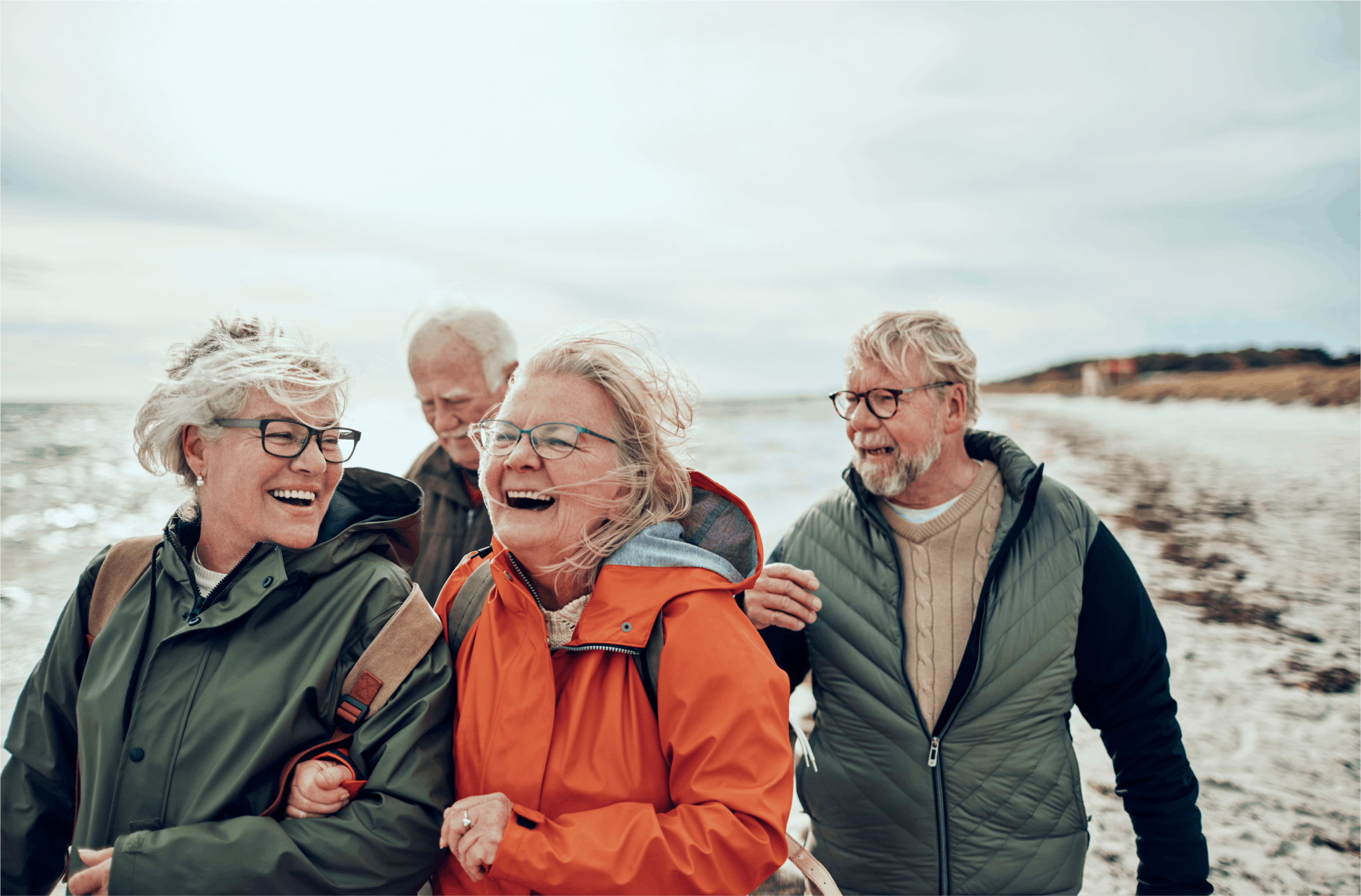 En grupp med fyra glada personer på en blåsig strand